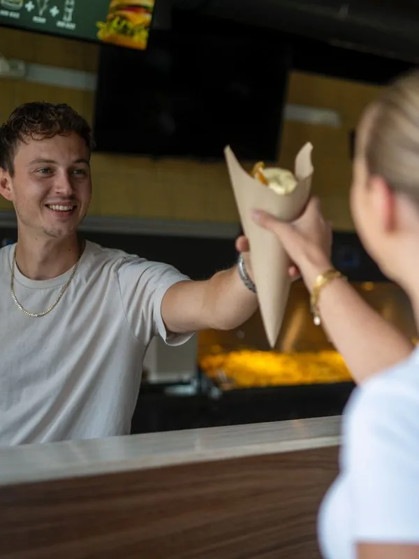 Medewerker van De Frietbar Julianadorp geeft een puntzak friet over de toonbank
